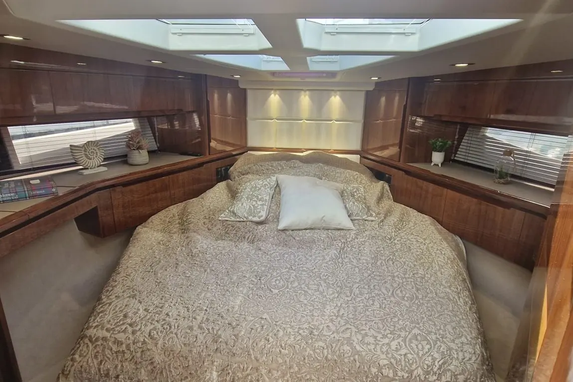 Luxurious boat interior with a large bed, ornate bedding, wooden cabinetry, and skylights providing natural light.